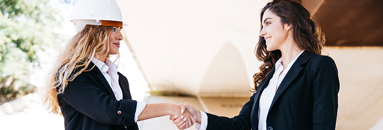 Image showing two young women shaking hands with each other. One of them is wearing a hard hat on her head.