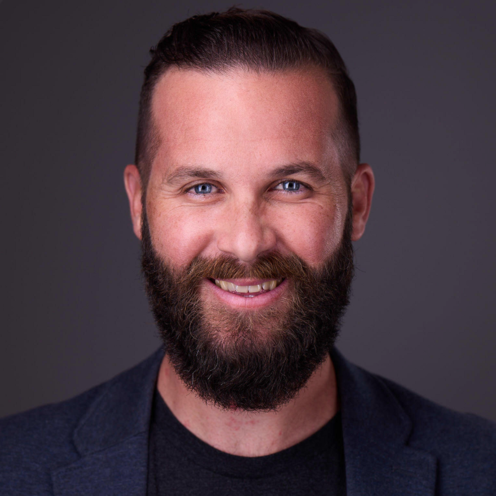 Headshot of Brett Farmiloe of Featured, wearing a black formal suit, full face beard and smiling at the camera
